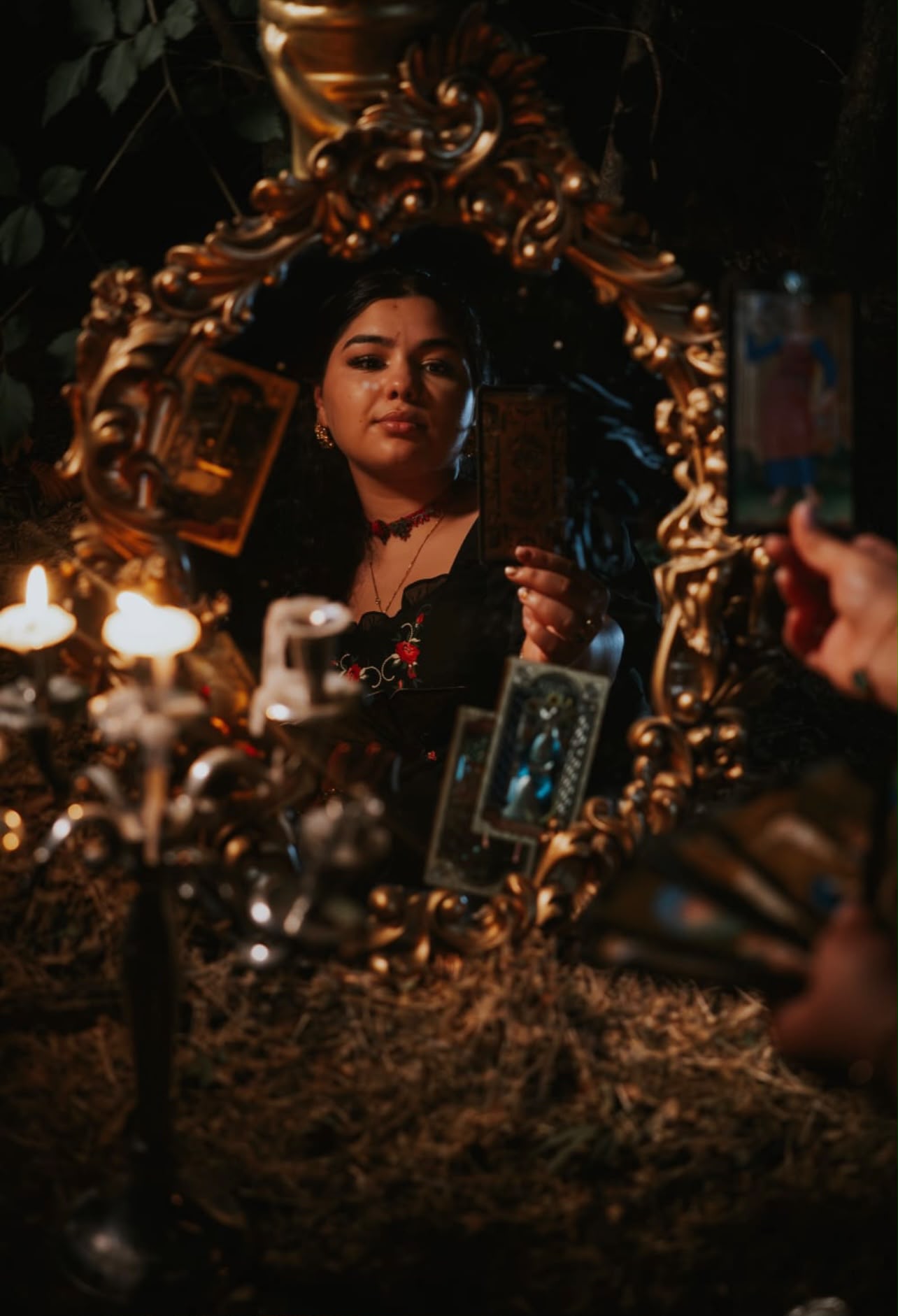 Vrăjitoarea Francesca reflectată într-o oglindă barocă aurie, ținând o carte de tarot la lumina lumânărilor