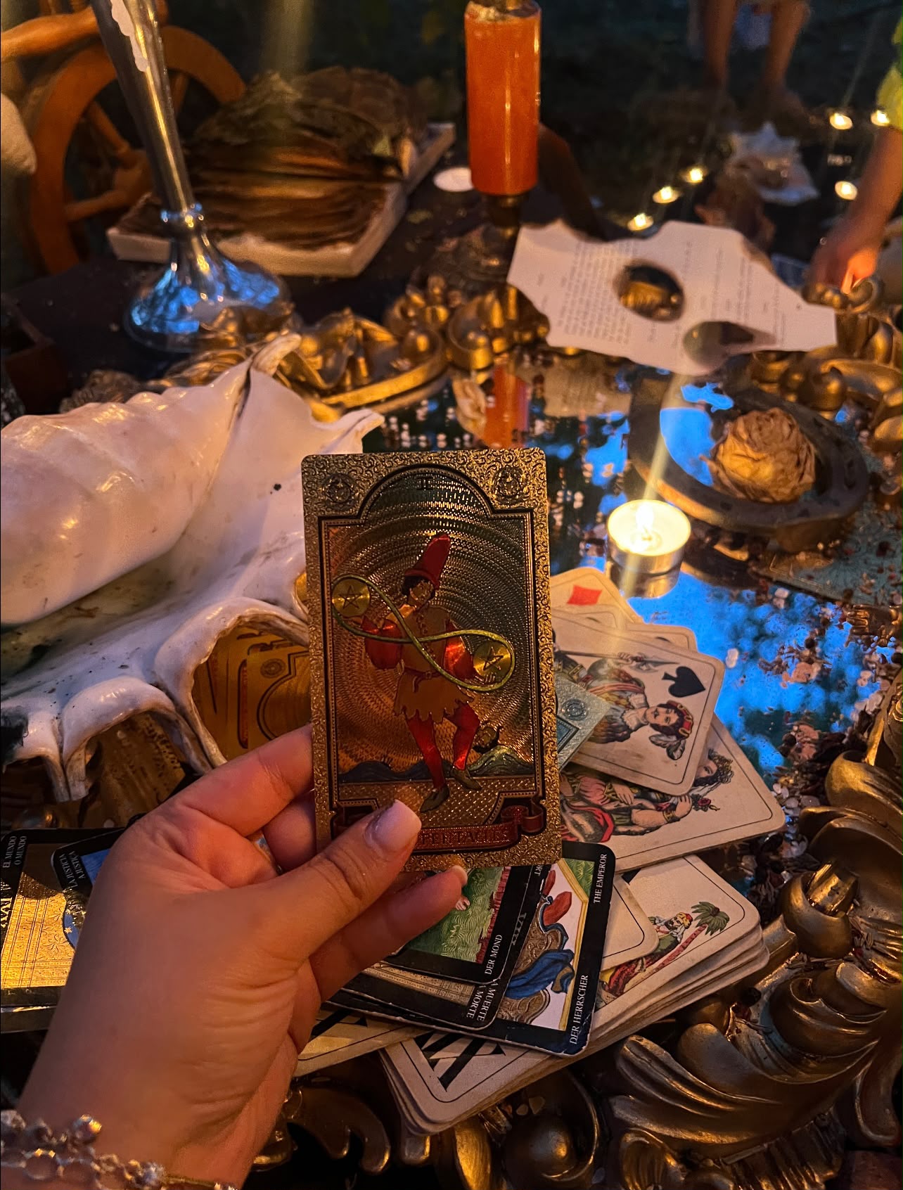 Mână care ține o carte de tarot deasupra unui altar cu lumânări și obiecte de ritual