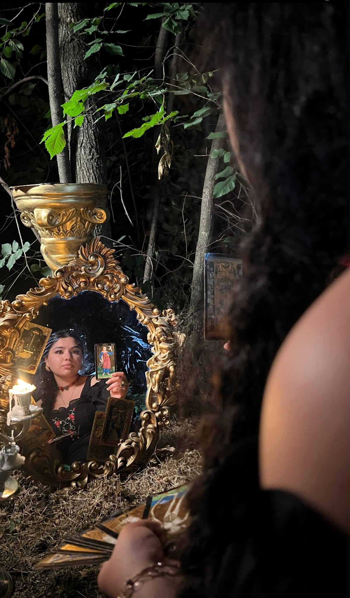 Francesca privindu-și reflexia în oglinda barocă din pădure, cu o carte de tarot în mână